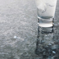 A greyish blue glossy stone surface with a glass on top